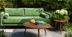 a green couch sitting next to a wooden table on top of a stone floor covered in greenery