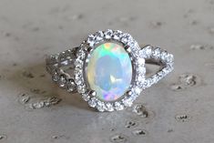 "A lovely Halo Setting featuring an oval-shape genuine top-notch Welo Opal with a magnificent play of color, complemented with a split shank embellished with pave set cubic zirconia handcrafted in Sterling Silver. Wrapped in a box ready for gift-giving.(r-egt-70 ) FINAL SALE Ring Info ----------------- *Opal measure 6mm x 8mm *Opal with Halo measure 11.5mm x 10mm *Ring Shank Width 2mm *Stone height 8mm *Model ring size 5 HOW TO CARE FOR YOUR OPAL --------------------------------------------- Opa Moissanite Opal Engagement Ring, Elegant Oval Opal Ring With Gemstone Accents, Classic Oval Opal Ring With Accent Stones, Oval Opal Ring With Accent Stones, Oval Opal Promise Ring, Dazzling Oval Opal Ring For Formal Occasions, Formal Oval Opal Ring With Gemstone Accents, Oval Opal Ring With Gemstone Accents For Anniversary, Oval Opal Ring With Halo Setting