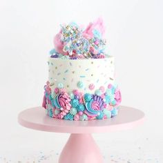 a multi layer cake with sprinkles and flowers on a pink stand against a white background