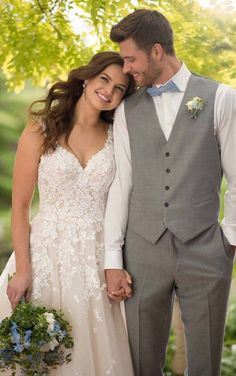 a bride and groom holding hands while standing under a tree in their wedding day attire