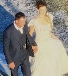 a man in a suit and tie walking next to a woman in a wedding dress