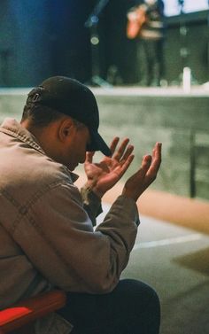 a man sitting in a chair with his hands up to his face while looking at the ground