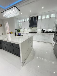 a large kitchen with marble counter tops and white cabinets in the center is illuminated by a crystal chandelier