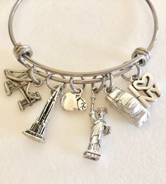 "New York City charm bangle with detailed pewter charms on stainless steel adjustable bangle. Fun detailed pewter charms of famous New York landmarks are 3D or two-sided made in USA and lead and nickel free. They include the Brooklyn Bridge, Empire State Building, apple, Statue of Liberty, taxi and \"I love NY\" charm. Adjustable bangle is made of high quality 1.8mm stainless steel and measures 2.5\" diameter to fit most sizes. Perfect souvenir of trip to NYC!" Adjustable Nickel-free Stainless Steel Bangle, Adjustable Stainless Steel Nickel-free Bangle, Nickel-free Metal Bangle Charm Bracelet, Adjustable Silver Bangle With Charms, Adjustable Antique Silver Metal Bangle, Silver Nickel-free Bracelet Souvenir, Nickel-free Silver Bracelets As Souvenir, New York Souvenirs, Ny Aesthetic