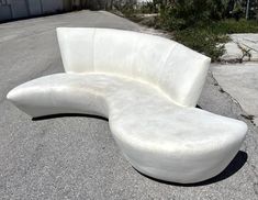 a curved white couch sitting on the side of a road