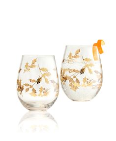 two wine glasses with gold leaf designs and an orange slice on the top one glass is half full