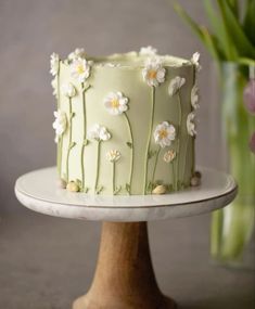 a green cake with white flowers on it sitting on a plate next to a vase