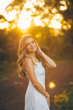 a beautiful young woman posing for a photo in front of the sun with her hand on her head