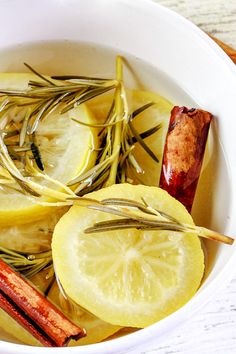 a white bowl filled with lemons and herbs next to cinnamon sticks on top of a wooden table