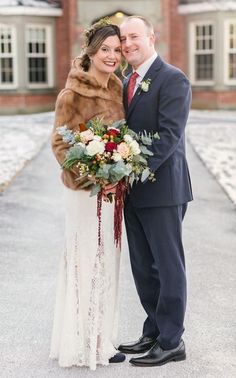 a bride and groom standing in front of a large brick building with snow on the ground