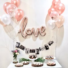 a table topped with cupcakes and balloons next to a love sign on the wall