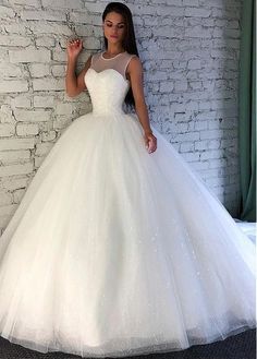 a woman standing in front of a brick wall wearing a white ball gown