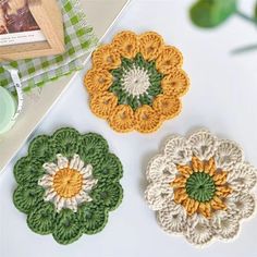 three crocheted flower coasters sitting on top of a table next to a cup