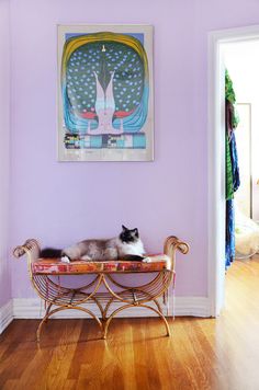 a cat laying on top of a bench in front of a painting hanging on the wall