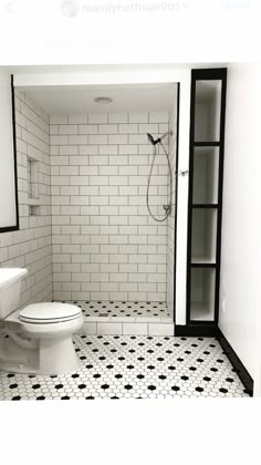 a white toilet sitting next to a shower in a bathroom under black and white tiles