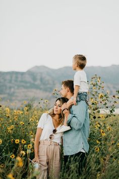 a man holding a child while standing next to a woman in a field with sunflowers