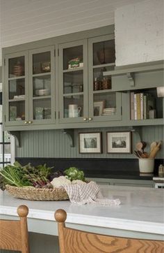 a kitchen filled with lots of green cupboards next to a white counter topped with vegetables