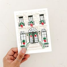 a hand holding up a card with an image of a house decorated for the holidays