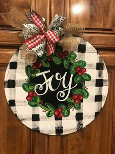 a door hanger with the word joy painted on it and holly wreath in front