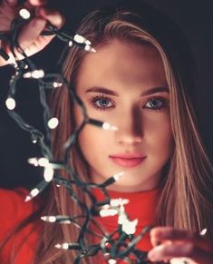 a beautiful young woman with long blonde hair and blue eyes is surrounded by christmas lights