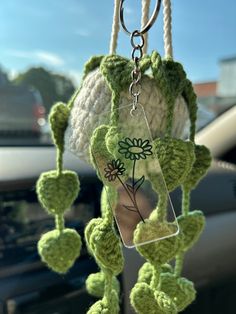 a green crocheted plant hanging from a car's rearview mirror holder with flowers attached to it