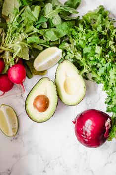 an avocado, radishes, and other vegetables on a marble surface