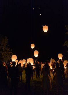 many people are flying lanterns in the dark