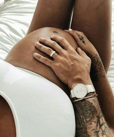 a tattooed woman laying on top of a bed next to a mans arm and wrist