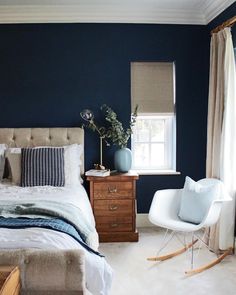 a bedroom with blue walls and white bedding, rocking chair in the foreground