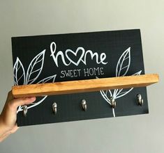 a person holding up a sign that says home sweet home with hooks on the wall