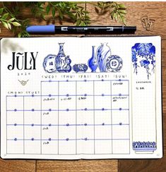 a calendar with blue vases on it next to a pen and some plants in the background