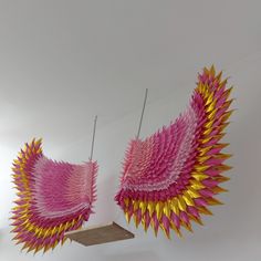 two pink and yellow paper sculptures hanging from hooks on the ceiling in a room with white walls