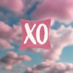 a pink pillow with the word xo on it floating in the air above clouds