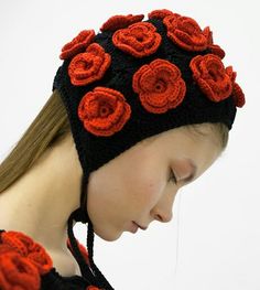 a woman wearing a black and red knitted hat with roses on the side, her eyes closed