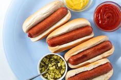 three hot dogs on buns with pickles and ketchup next to them