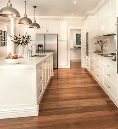 a large kitchen with white cabinets and wood flooring on the walls, along with stainless steel pendant lights