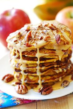 a stack of pancakes covered in icing and pecans on a plate next to apples