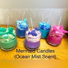 four different colored candles sitting on top of a wooden table with the words mermaid candles ocean mist scent