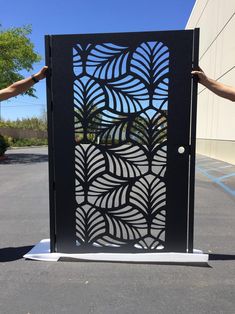 two people are holding up an intricate metal door with blue leaves on the side and one person's hand reaching for it