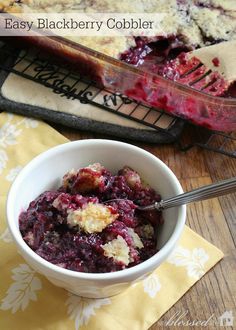 blueberry cobbler in a white bowl with a serving spoon next to it on a yellow napkin