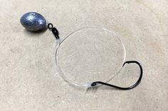 a fishing hook with a ball on the ground next to it and a black string