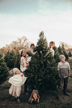 four children are standing in front of a christmas tree and one is holding the top