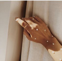 a woman's hand with white pearls on her left arm and the curtain behind her