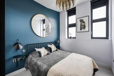 a bedroom with blue walls and white carpeted flooring, a round mirror above the bed