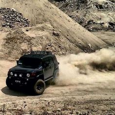 a black vehicle driving on top of a dirt road next to a pile of rocks