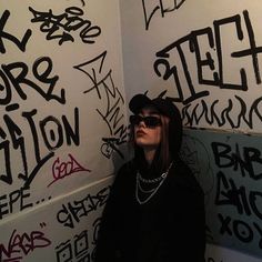 a woman wearing sunglasses and a black hoodie standing in front of graffiti covered walls