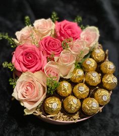 pink roses and chocolates in a bowl on a black surface with some gold foil