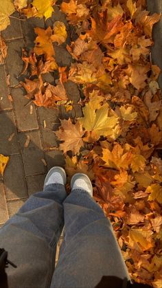 the person is standing in front of leaves on the ground with their legs crossed and feet propped up