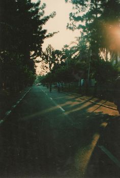 the sun shines brightly on an empty street with trees in the foreground and people walking down the sidewalk