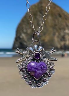 The charoite cabochon heart is surrounded with decorative and patterned wire, two sterling silver swallow birds, silver flower with an amethyst center sitting at the top of the pendent, and seven tiny amethyst stones. The silver back plate is signed by me. The Charoite stone is known to help release negative energy and fears, as well as protection and healing. Pendant is two inches long by 2 inches wide. Chain measures 26 inches long. Purple Sterling Silver Heart Jewelry, Purple Artisan Sterling Silver Jewelry, Artisan Sterling Silver Purple Jewelry, Purple Heart Sterling Silver Jewelry, Artisan Purple Sterling Silver Jewelry, Artisan Sterling Silver Jewelry In Purple, Purple Amethyst Jewelry With Heart Charm, One Of A Kind Purple Pendant Jewelry, Silver Amethyst Jewelry With Heart Charm